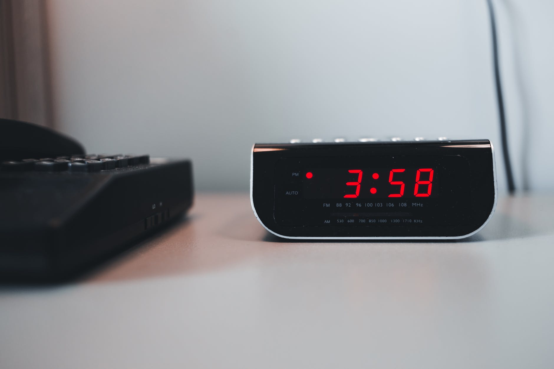 digital alarm clock beside a telephone on a white surface